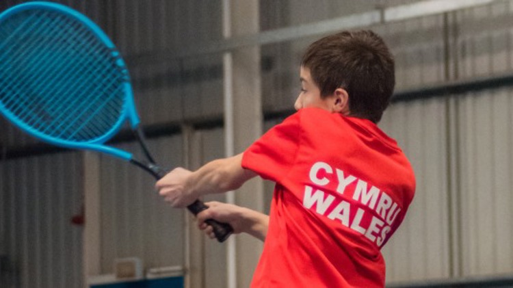 Aiden Coopman returning a shot in an indoors tennis match