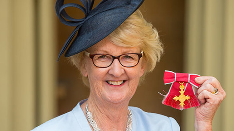 Cathie Sabin honoured with an OBE in 2016, holding it up to the camera