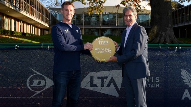 two men hlding gold standard ITF trophy between them outside the LTA building