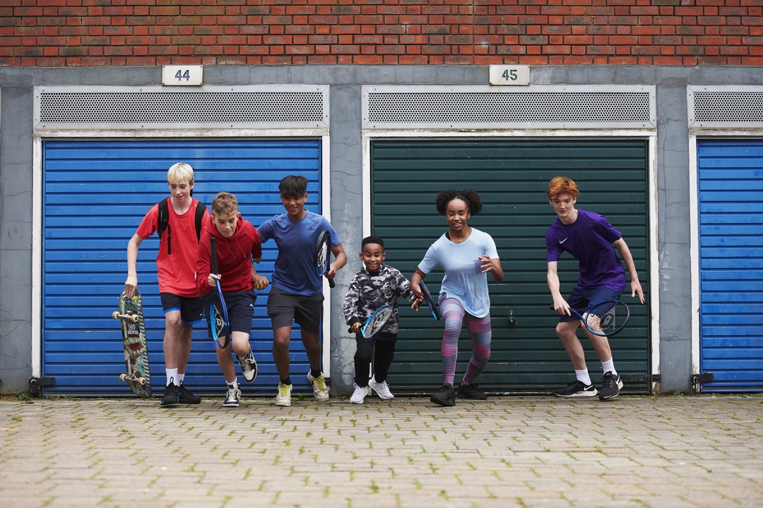 Kids holding tennis rackets running with colourful garage doors in background