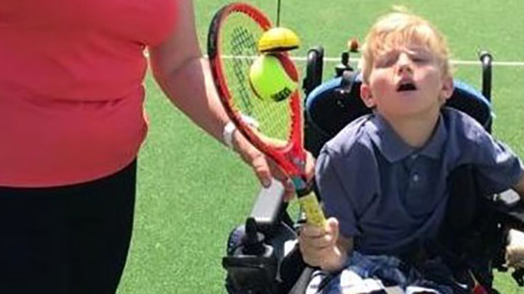 Young disabled boy playing tennis with a tennis coach