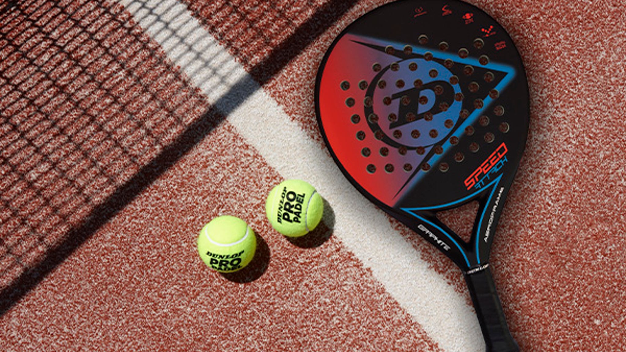 Two padel balls and a Dunlop padel bat on a clay-coloured padel court