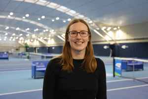 LTA colleague Maddi Mclean standing in front of the indoor hard courts at the National Tennis Centre