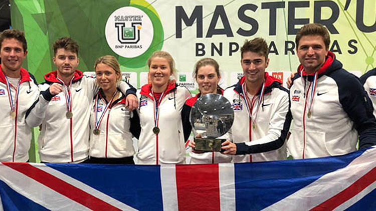 GB unviersity team standing in a line with medals and holing a trophy and holding big GB flag at the front