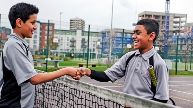 Two boys shaking hands at a tennis net