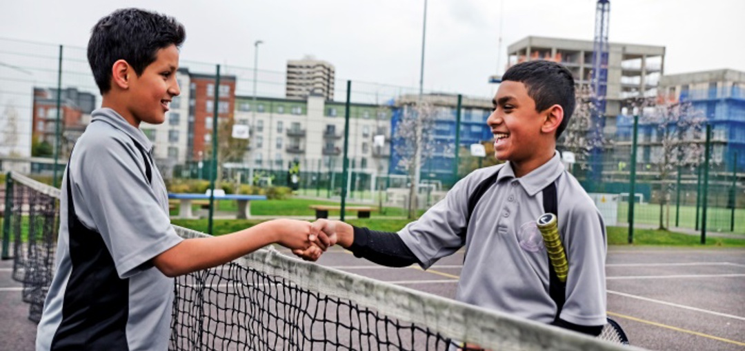 Two boys shaking hands at a tennis net