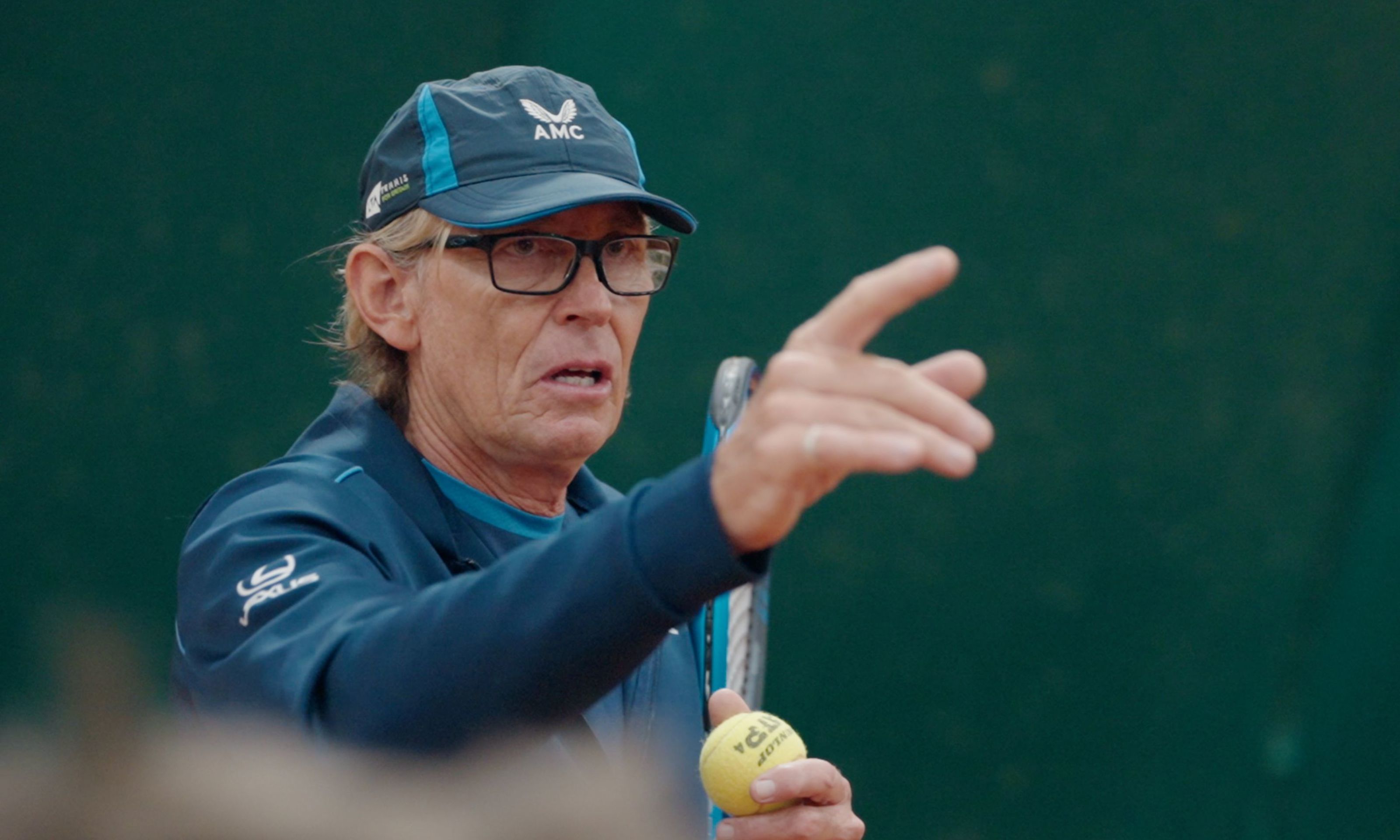 Coach, Richard Plews pointing while holding a racket and ball