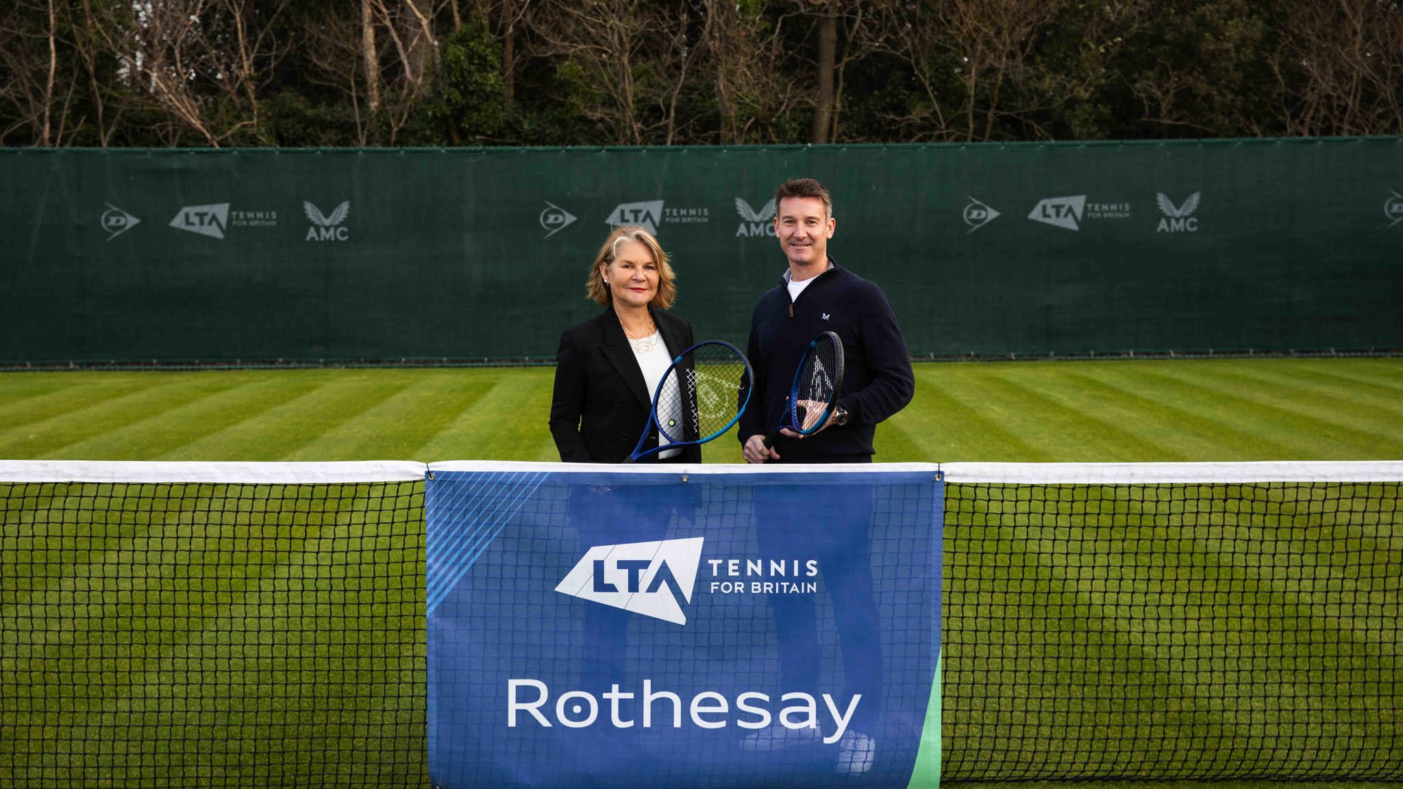 A male and female holding rackets and standing behind a tennis net