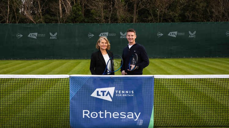 A male and female holding rackets and standing behind a tennis net