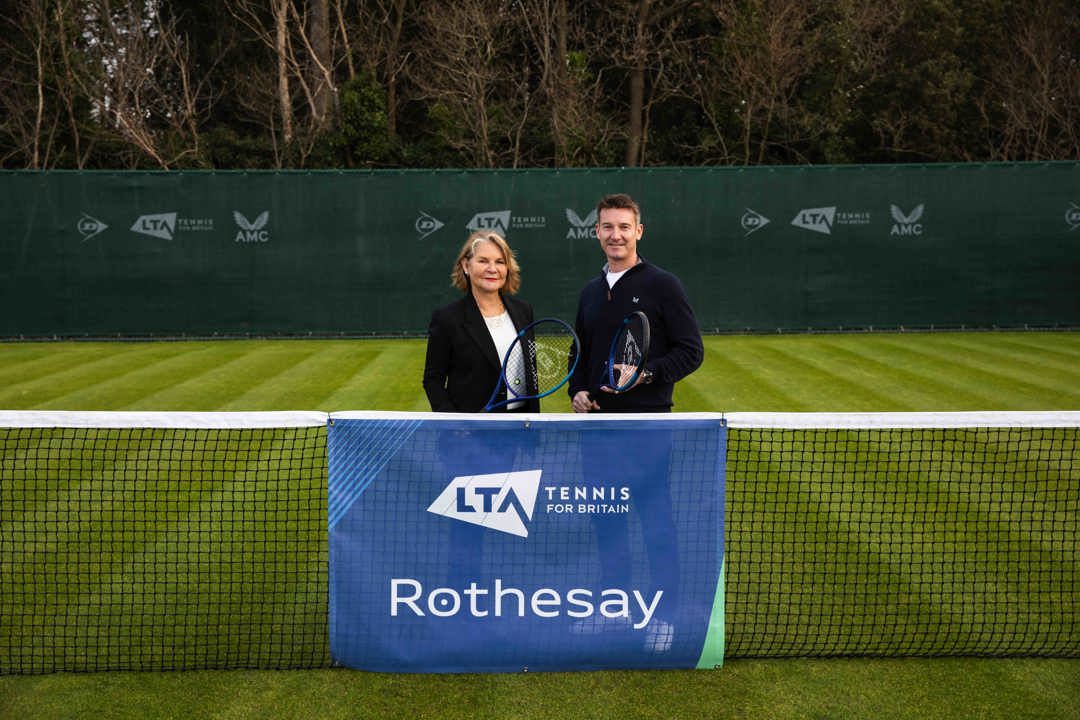 A male and female holding rackets and standing behind a tennis net