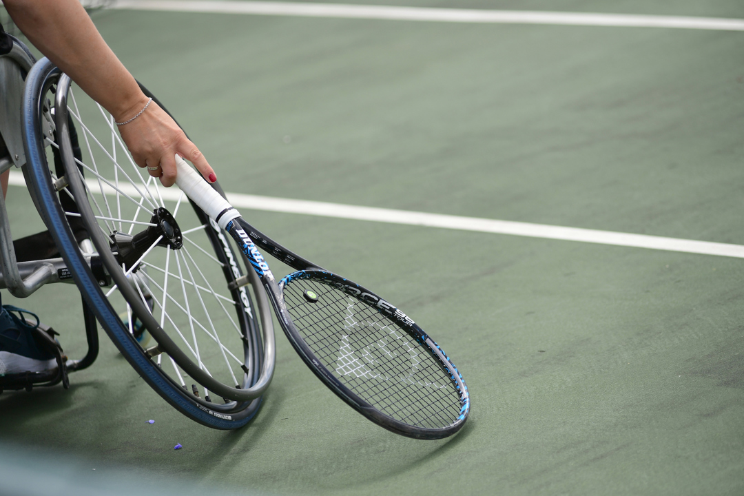 Close-up image of wheelchair on court with a tennis racket