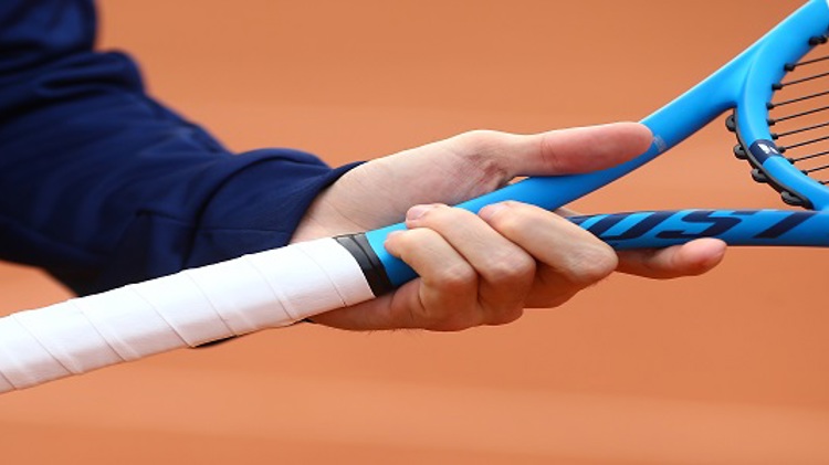 A person holding a blue tennis on a clay tennis court racket