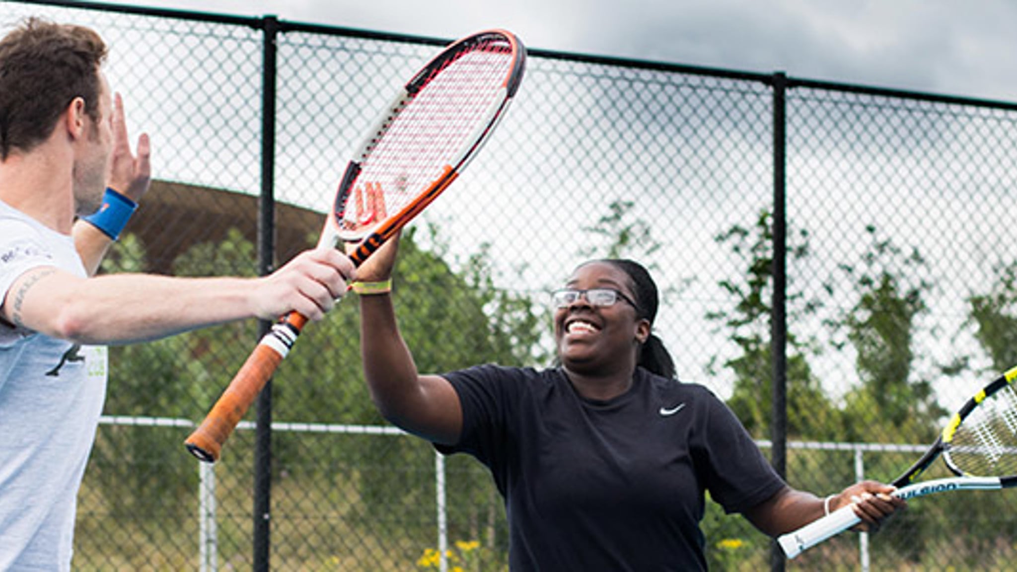 Two people high fiving while playing tennis with courtside fence in background