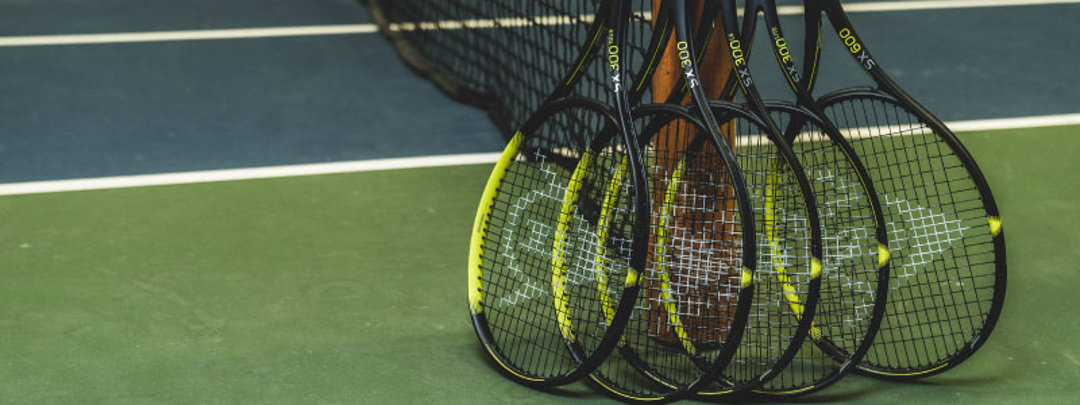 image of 5 black and yellow tennis dunlop  rackets leaning against a tennis net