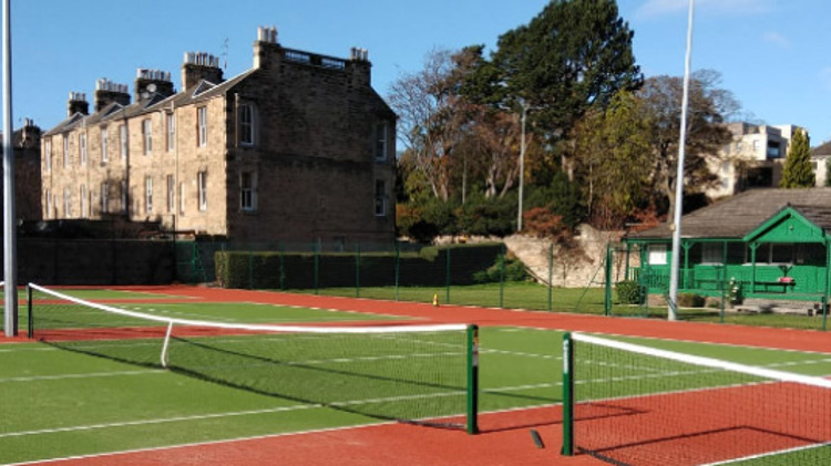 4 artificial grass courts with a wooden pavilion at the back  of the courts and houses to left