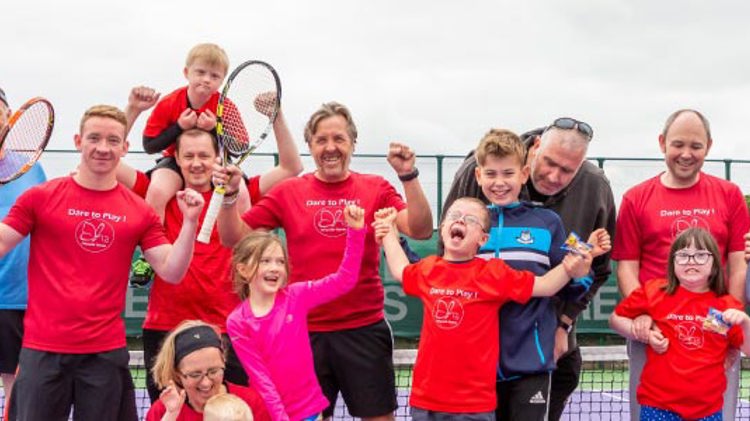 adults and kids lined up in front of a tennis net laughing and smiling for a photo