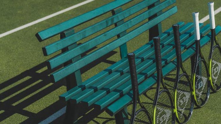 yellow and black dunlop tennis rackets lined up against a green bench on tennis court