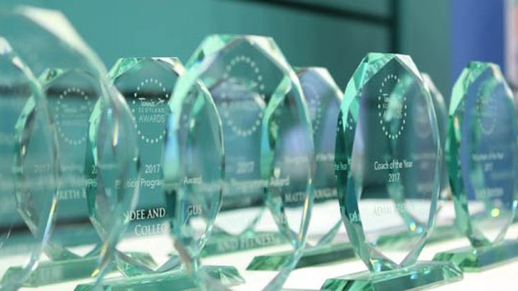 10 clear glass trophies with inscriptions for different awards placed on a table  