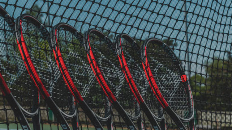 close up of 6 dunlop black and red tennis rackets placed  leaning on tennis net