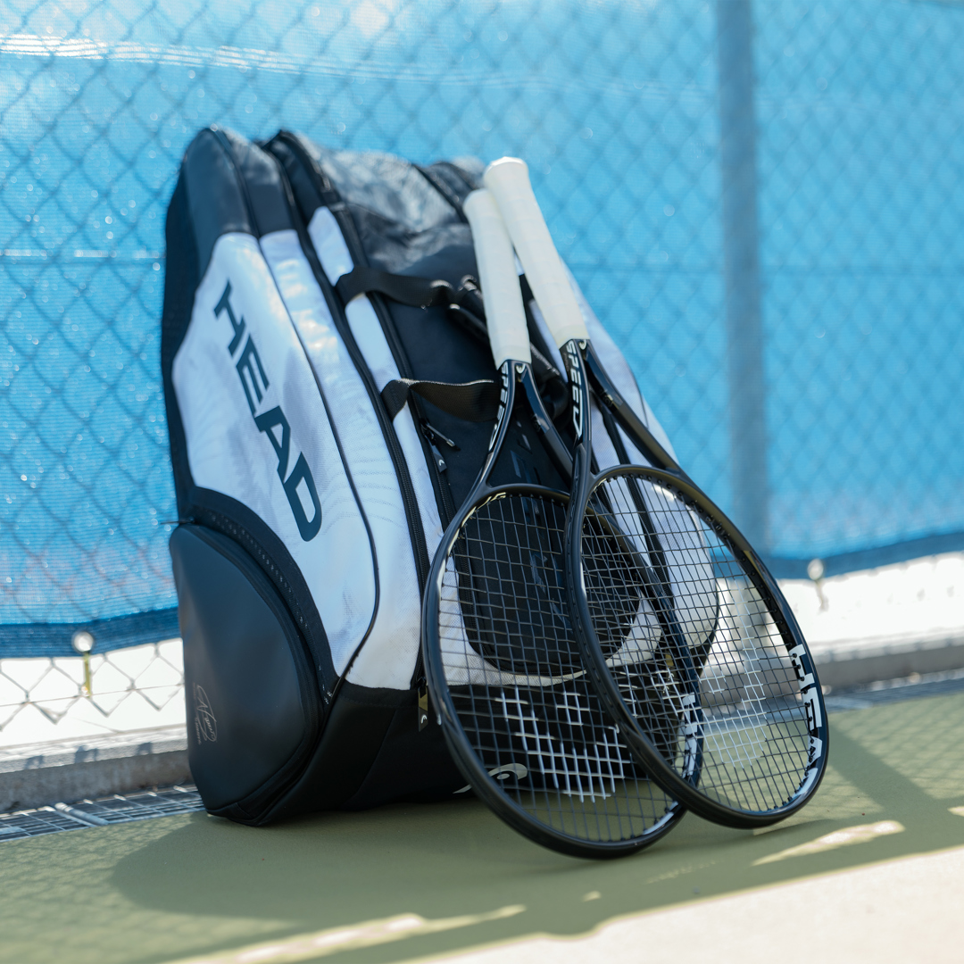 Two tennis rackets leaning against a tennis bag against the court fence. 