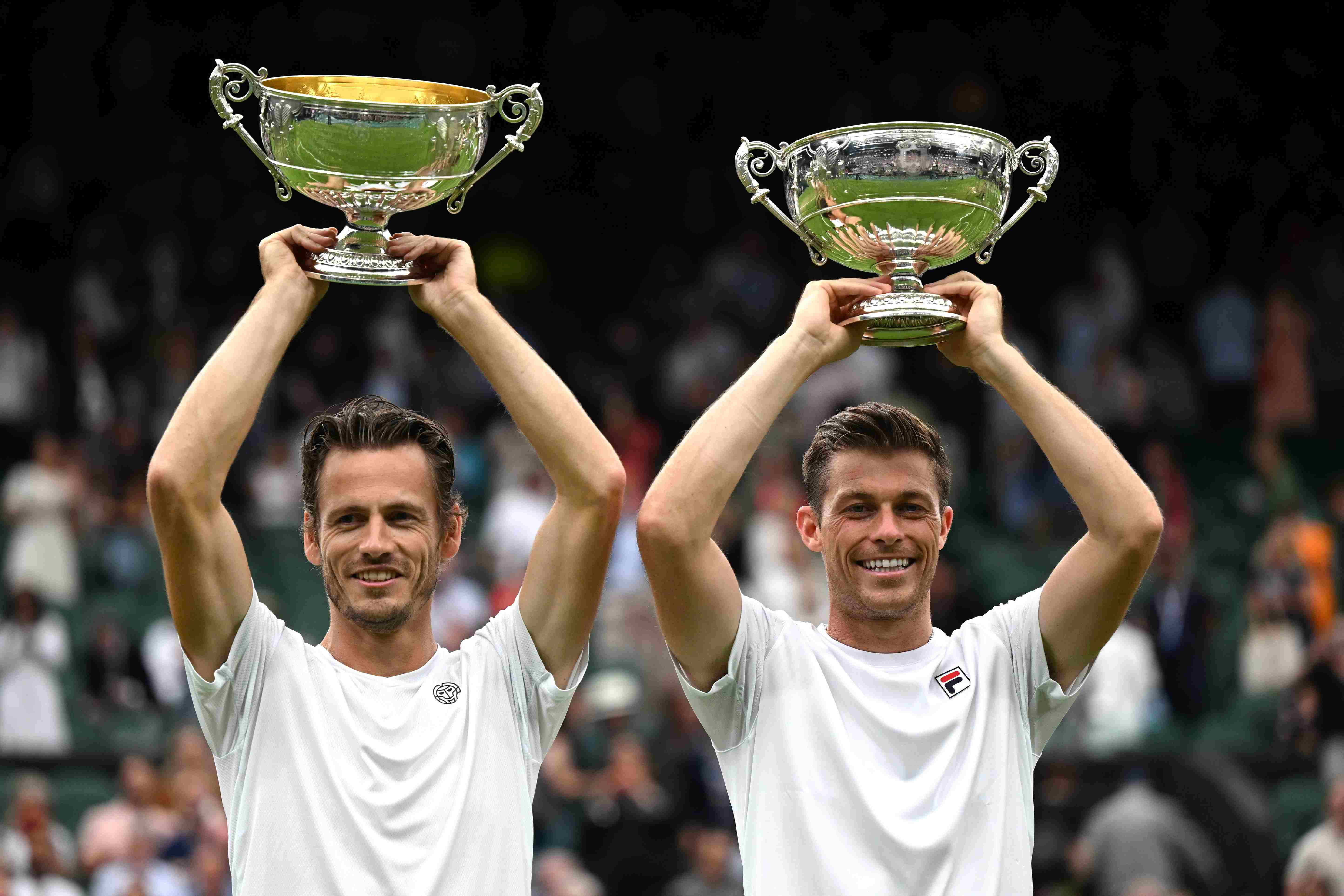 Neal Skupski and Wesley Koolhof lifting their championship trophies above their heads on court at Wimbledon