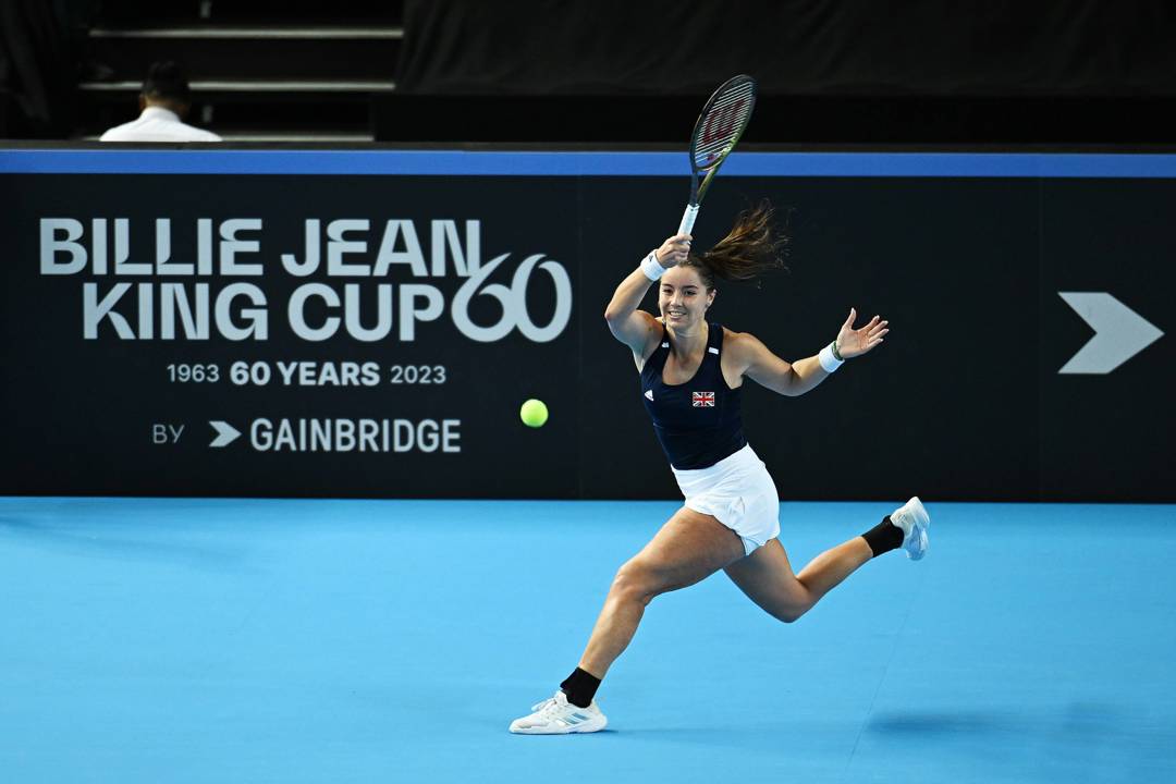 Jodie Burrage hitting a forehand on court in front of a Billie Jean King Cup advertisement board at the Copper Box Arena