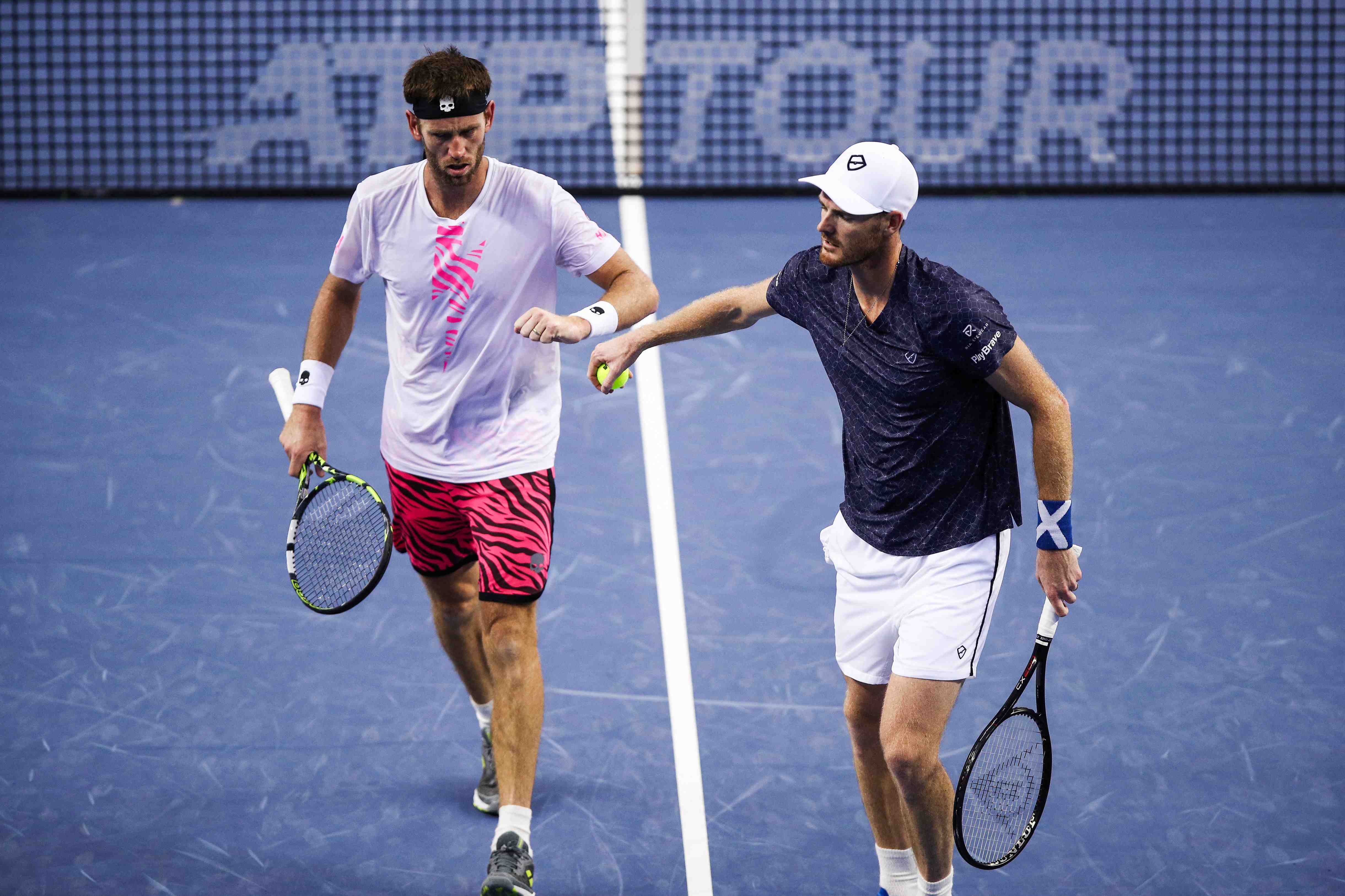 Jamie Murray and Michael Venus stood fist bumping on court with an ATP Tour branded tennis net behind them