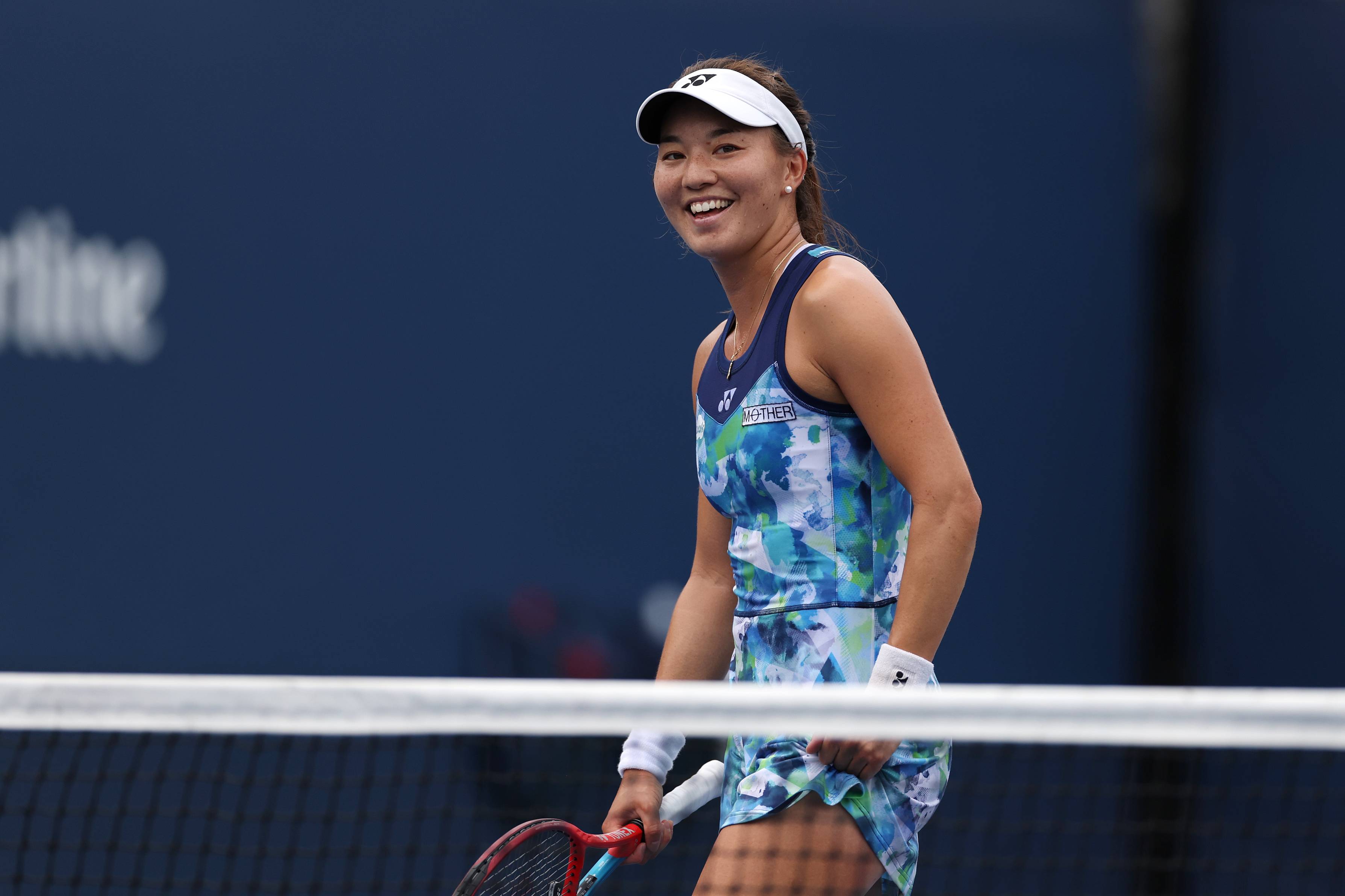 Lily Miyazaki smiling and holding her tennis racket on court at the US Open