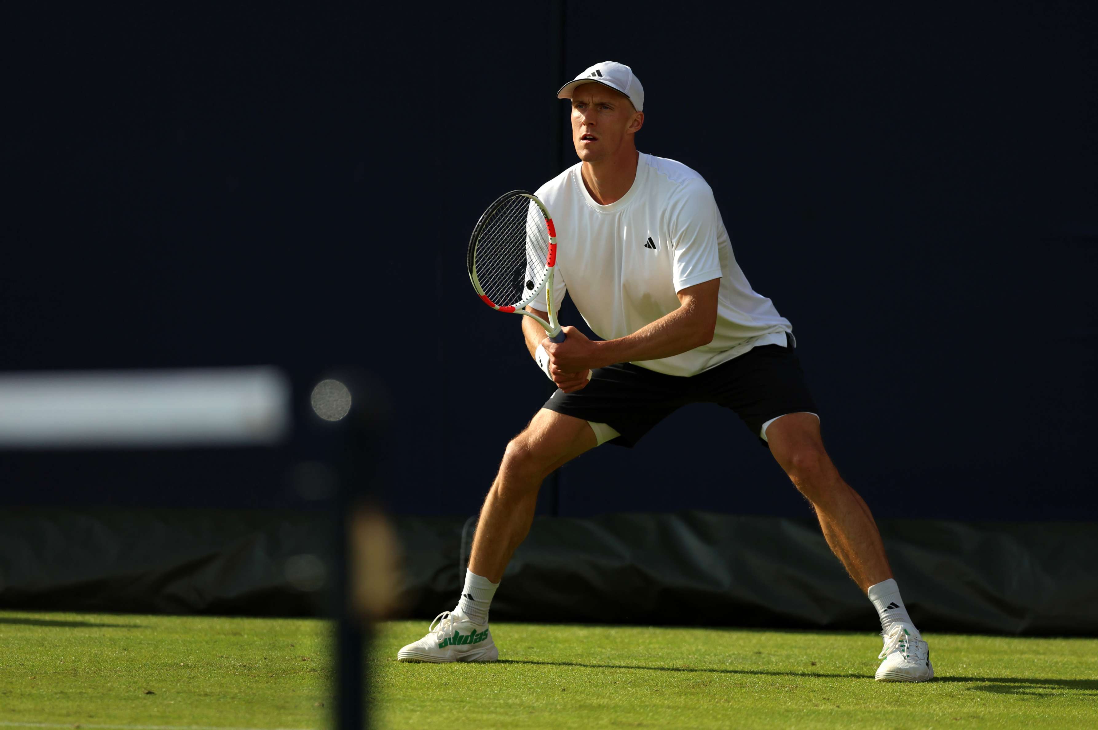 British tennis player crouching down and preparing to return a serve on a grass court
