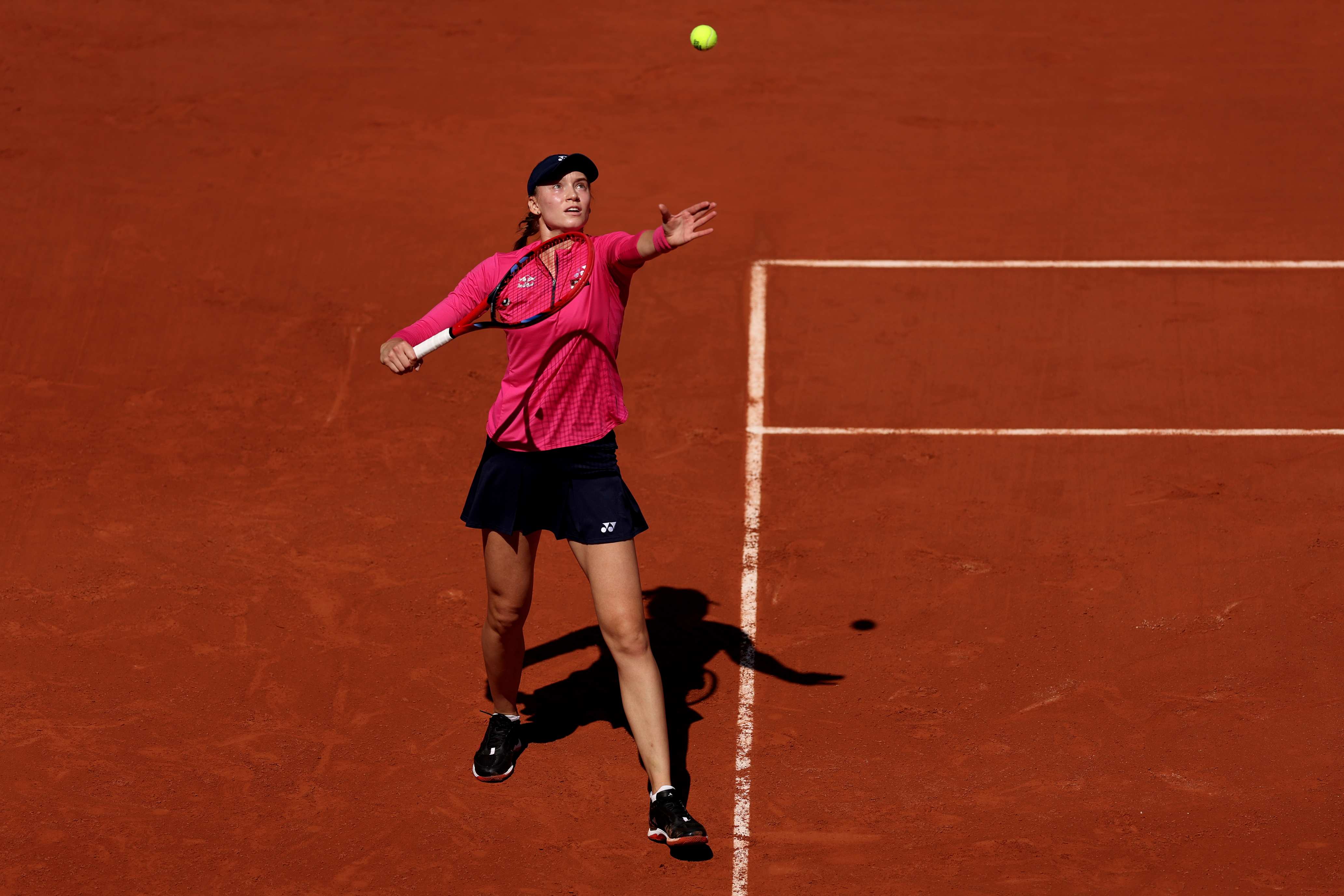 Elena Rybakina stood on a clay court while throwing a tennis ball in the air as she prepares to serve