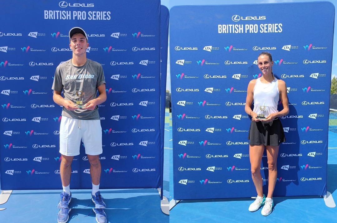 Two people, one man and one woman, stood holding glass trophies in front of a large blue board with small sponsor logos on it