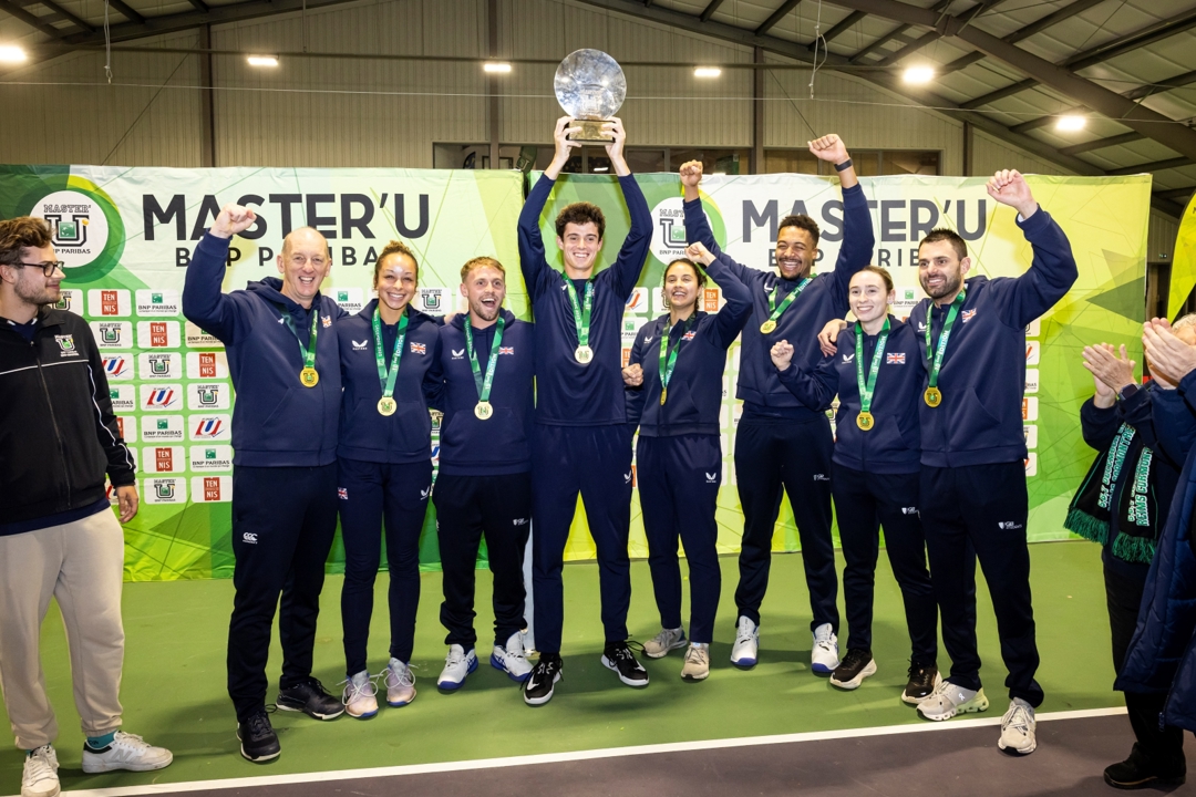 A group of men and women smile and raise their hands in the air in celebration. In the middle of the group, a man holds aloft a glass trophy. 