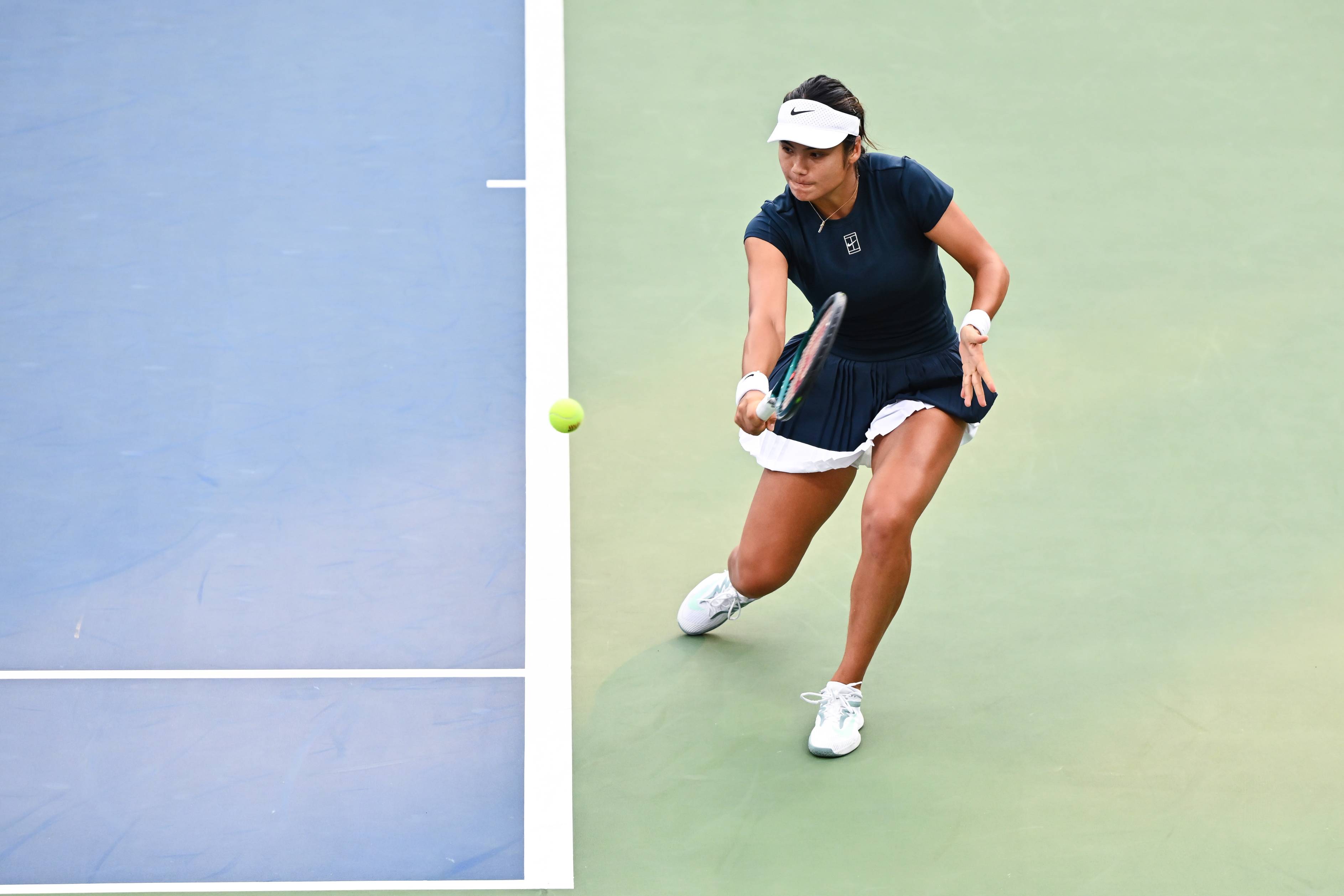 Emma Raducanu hitting a backhand from behind the baseline on a hard court