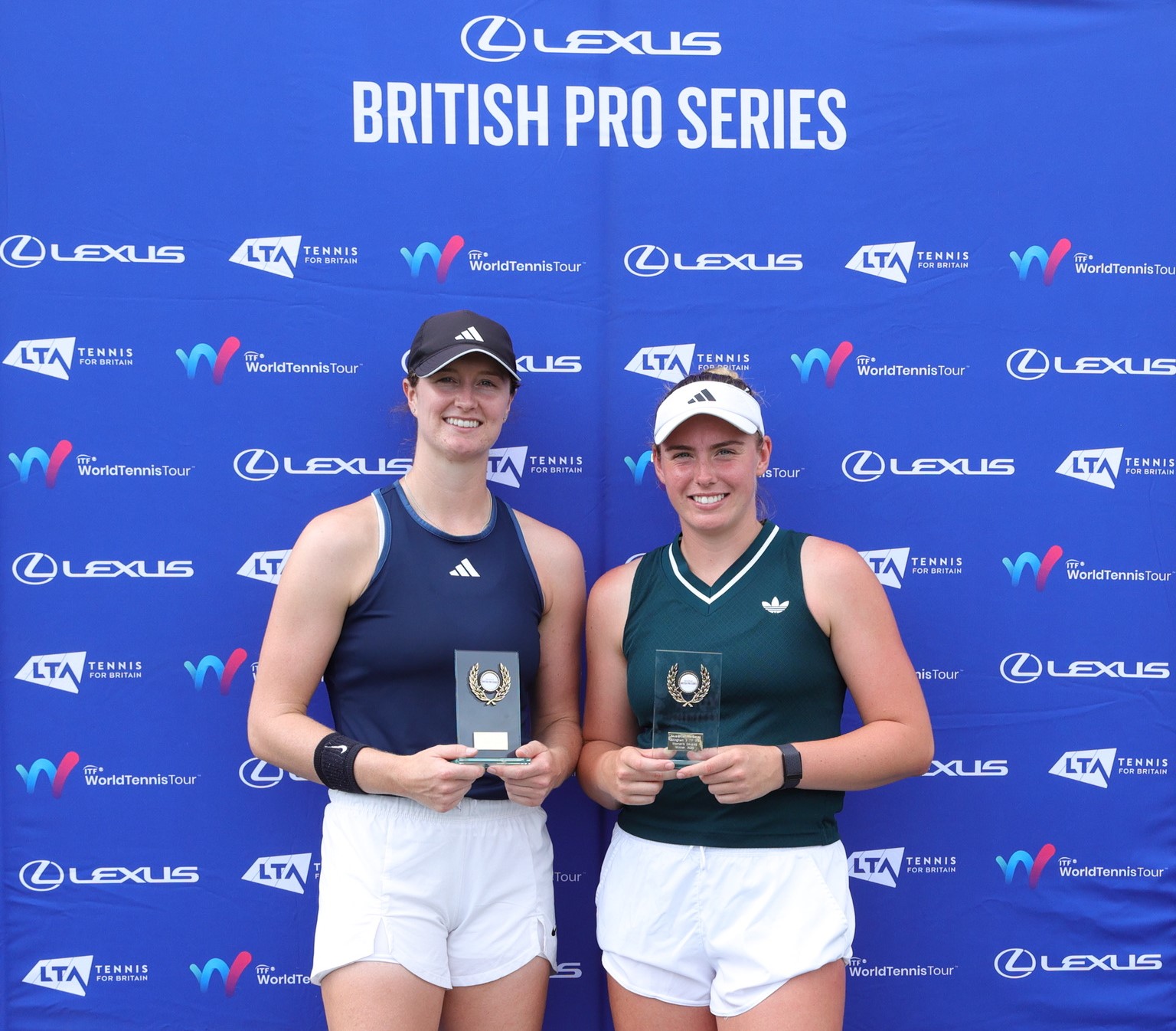Two women stand in front of a blue background holding glass trophies. ABove them read the words, 'Lexus British Pro Series'