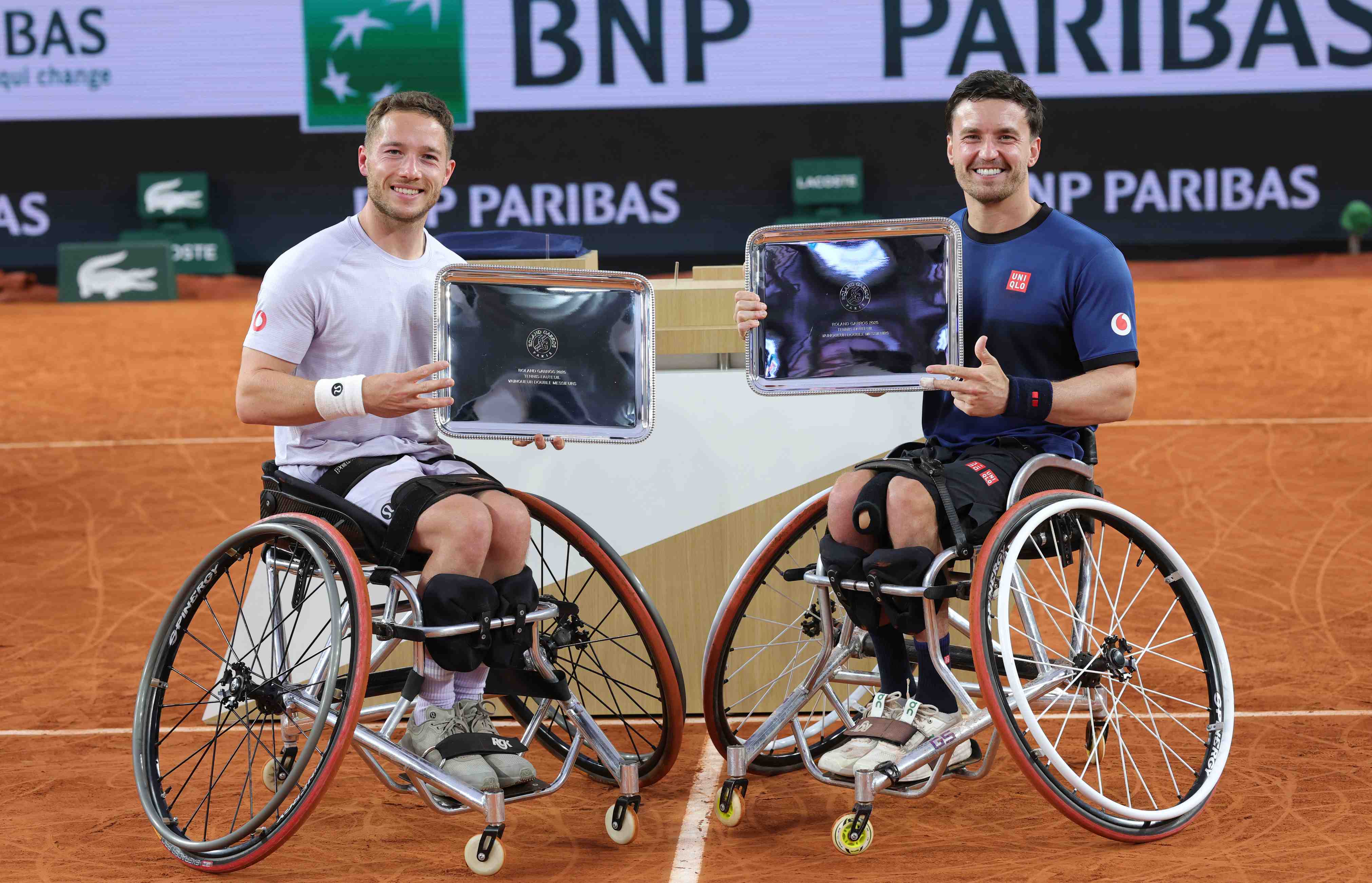 Alfie Hewett and Gordon Reid smiling while holding their winners trophies at Roland Garros