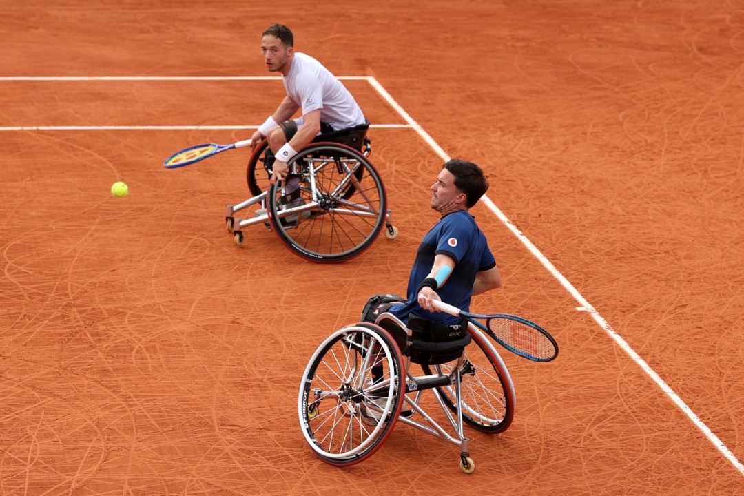 Gordon Reid about to hit a forehand on the clay with his partner Alfie Hewett looking on