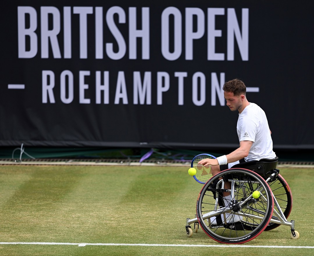 Alfie Hewett bouncing the ball before a serve on grass in front of the Lexus British Open sign