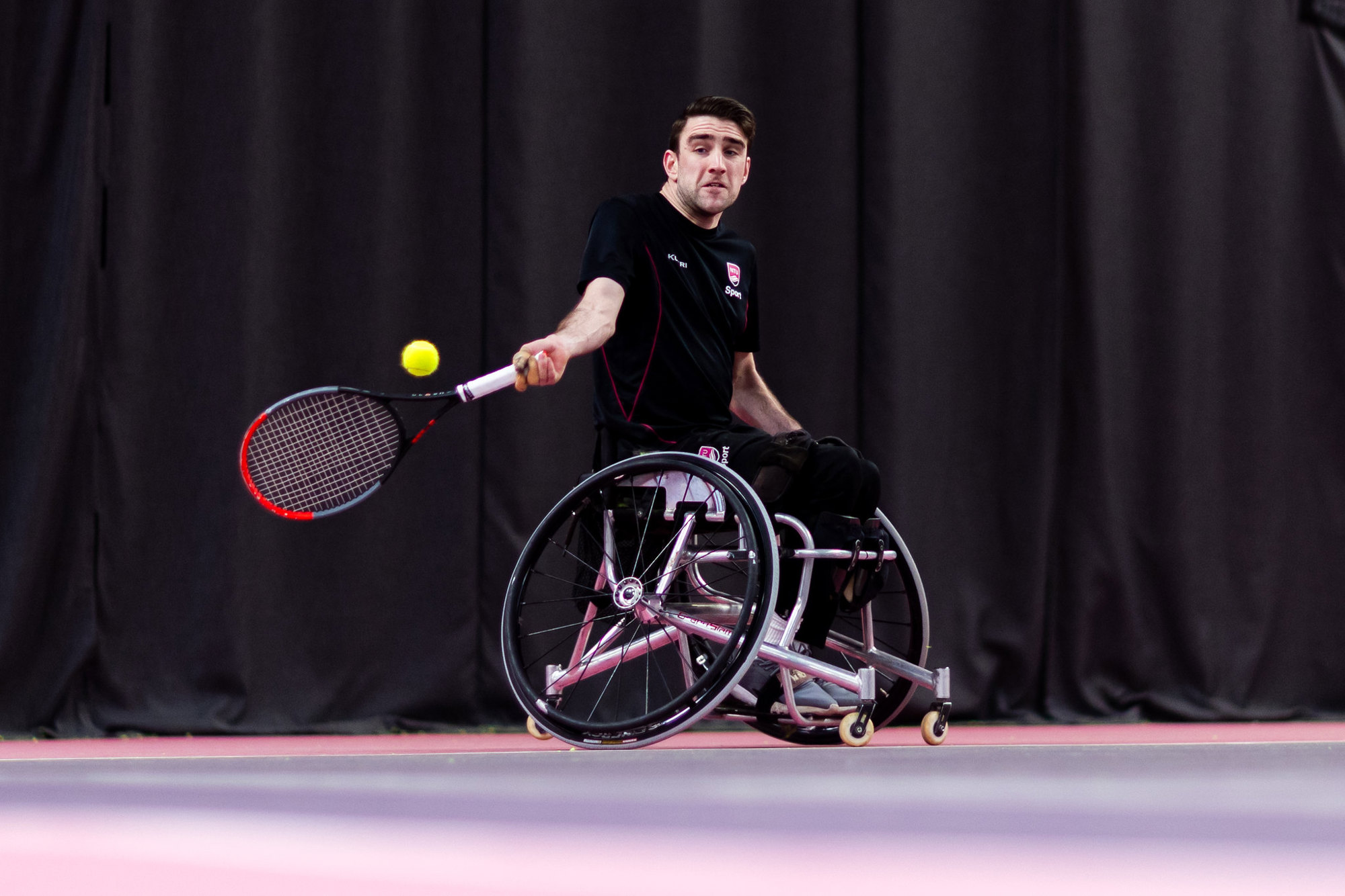 A man in a wheelchair hits a tennis ball