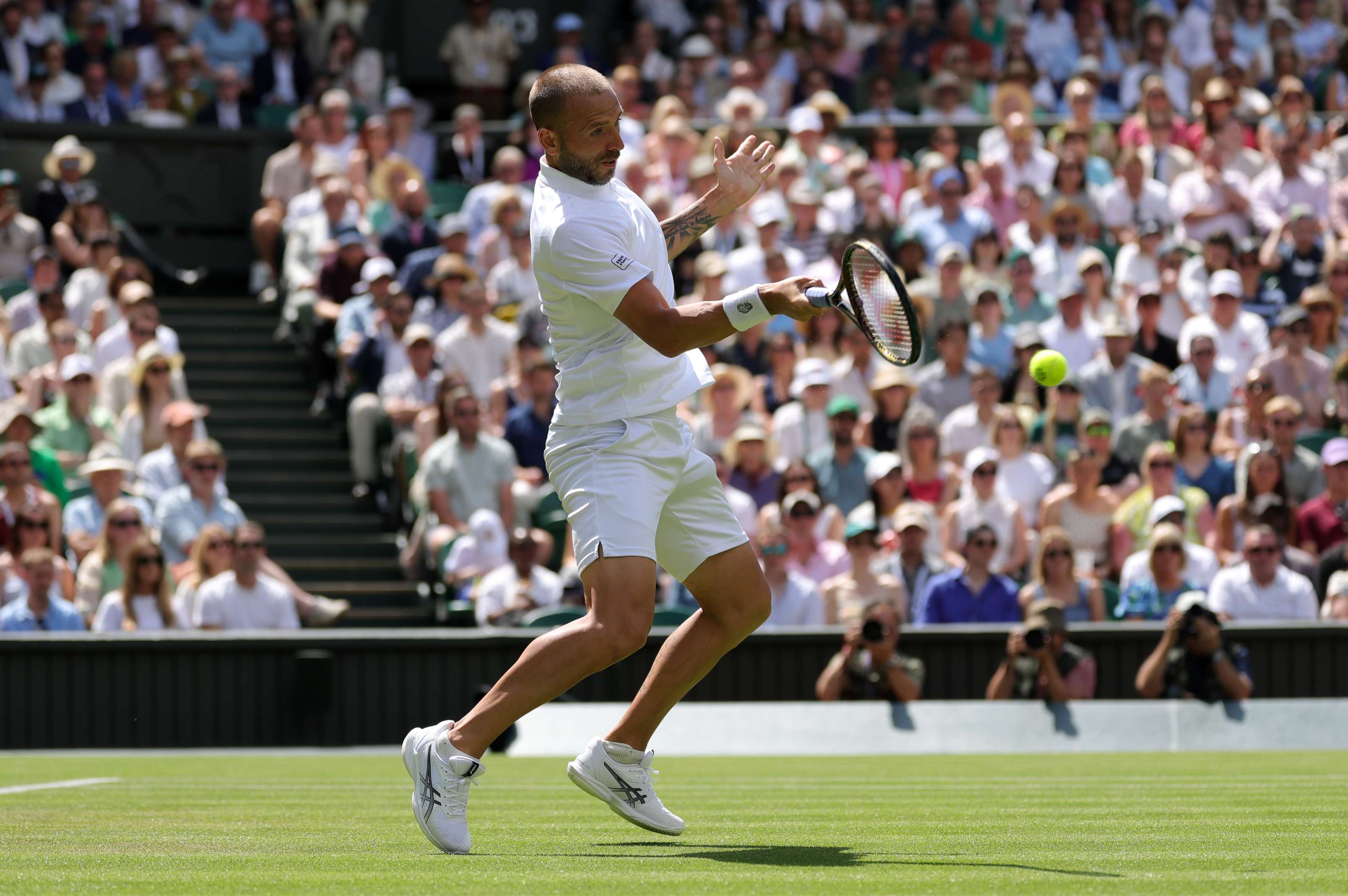 British tennis player Dan Evans hitting a forehand on Centre Court at Wimbledon during his second round match against Novak Djokovic 