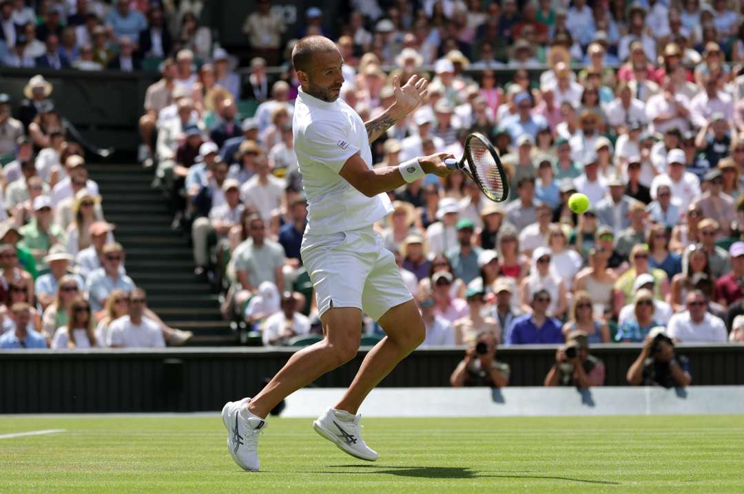 British tennis player Dan Evans hitting a forehand on Centre Court at Wimbledon during his second round match against Novak Djokovic 