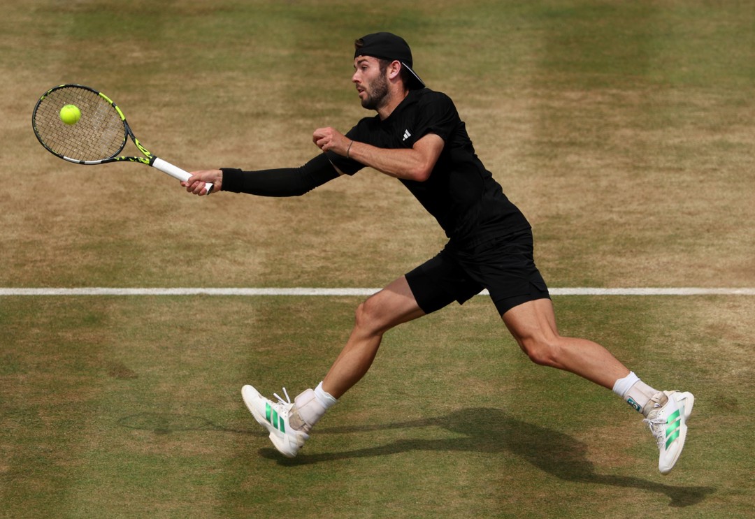 Jacob Fearnley reaches to hit a ball with his racket on a grass court