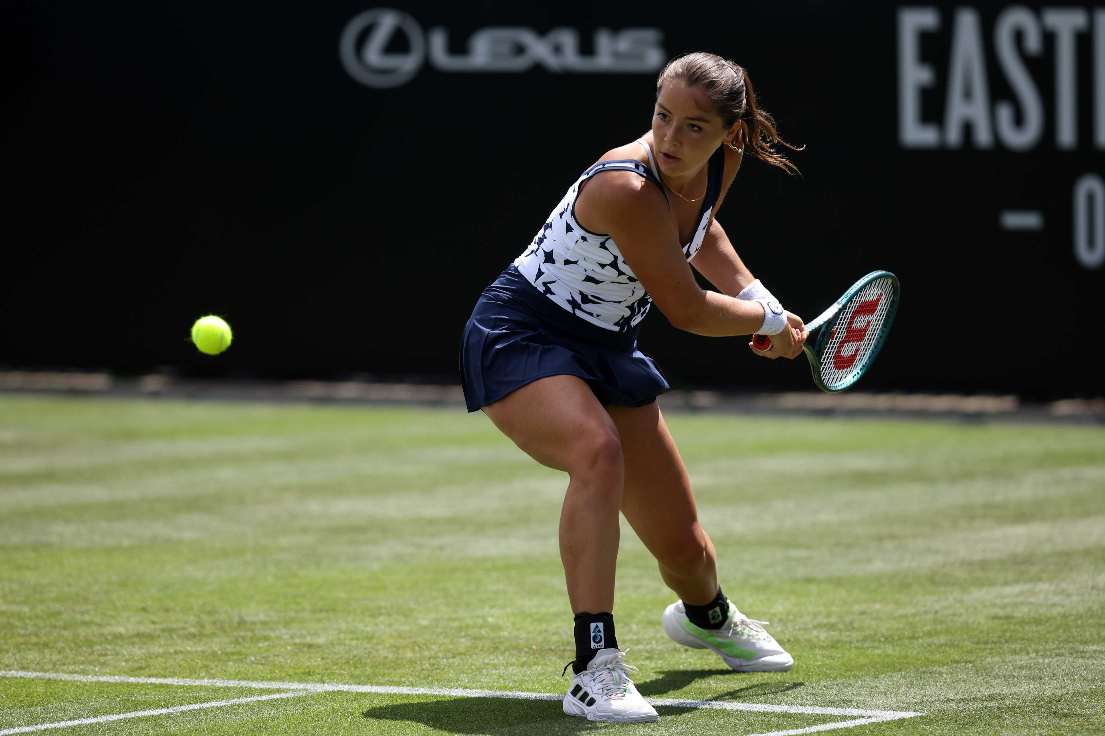 Jodie Burrage bending down low on a grass court in preparation of hitting a backhand
