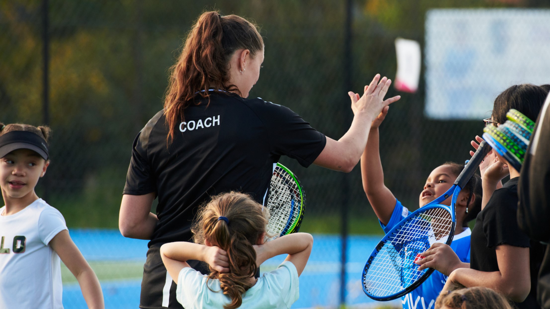 A female coach high fiving a young girl with tennis rackets in their hand