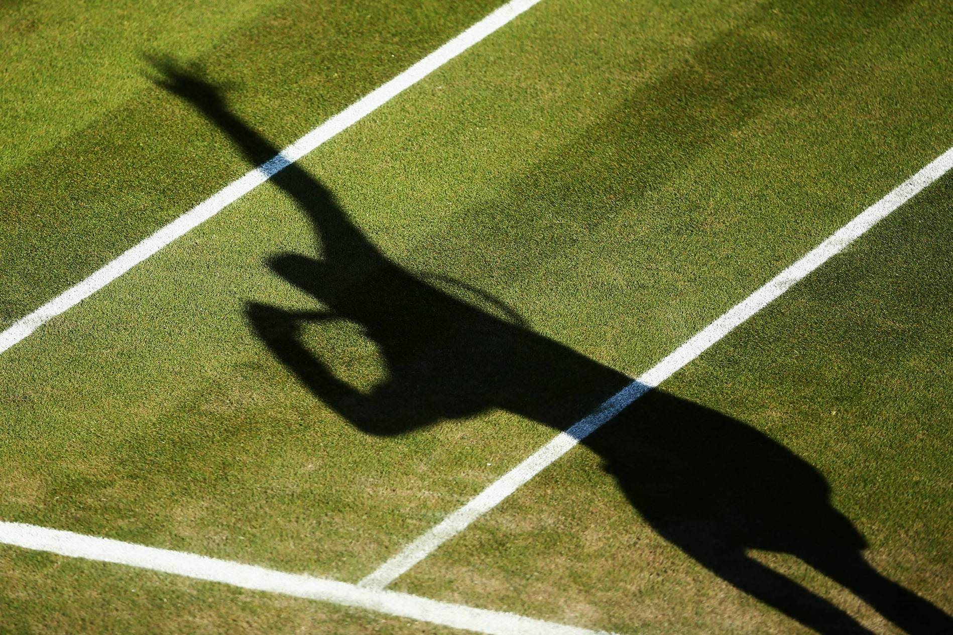 Shadow of a tennis player serving on the grass