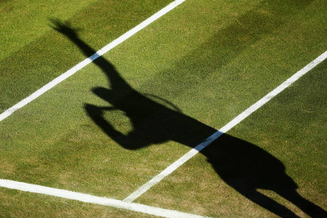 Shadow of a tennis player serving on the grass