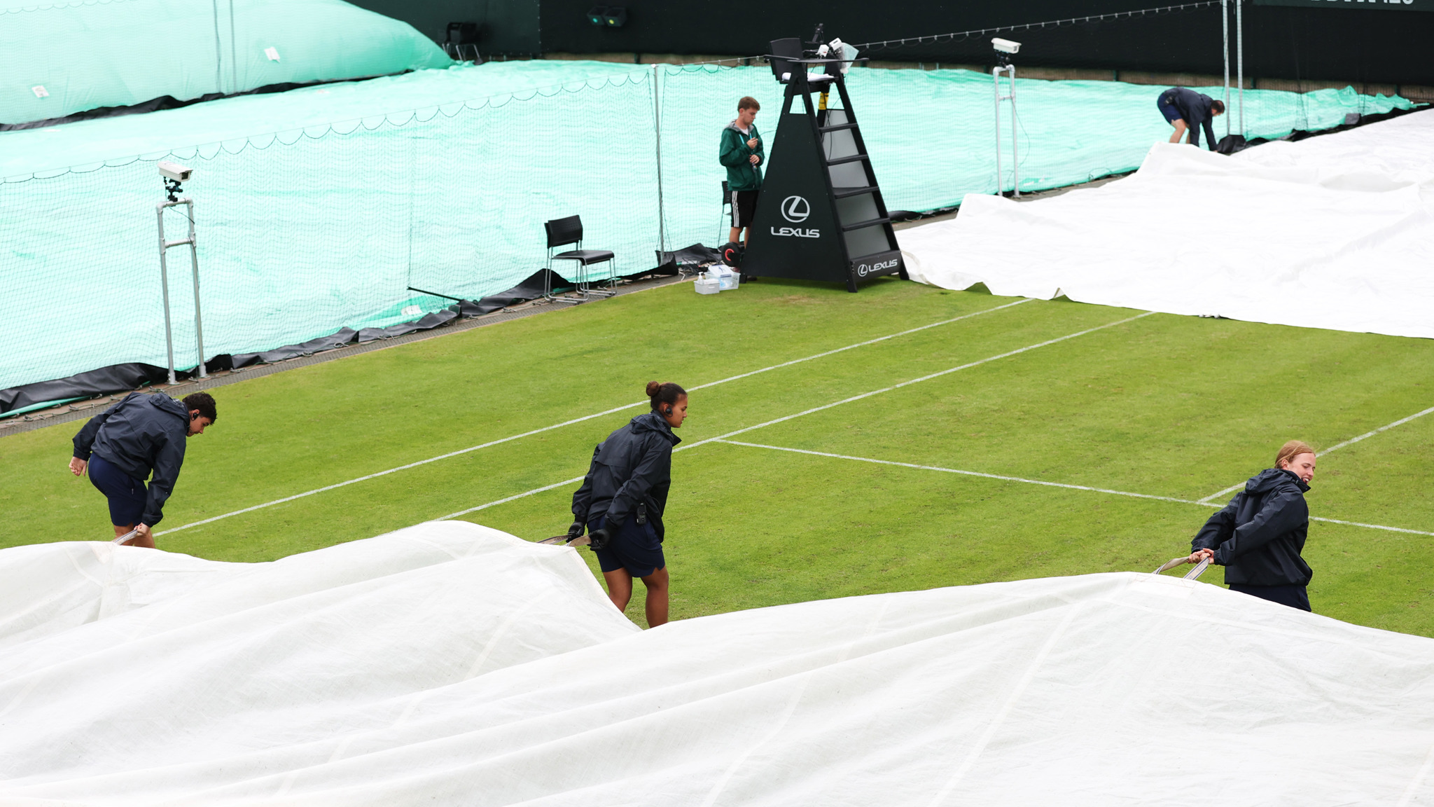 Three grounds staff pull the covers over the court during the rain