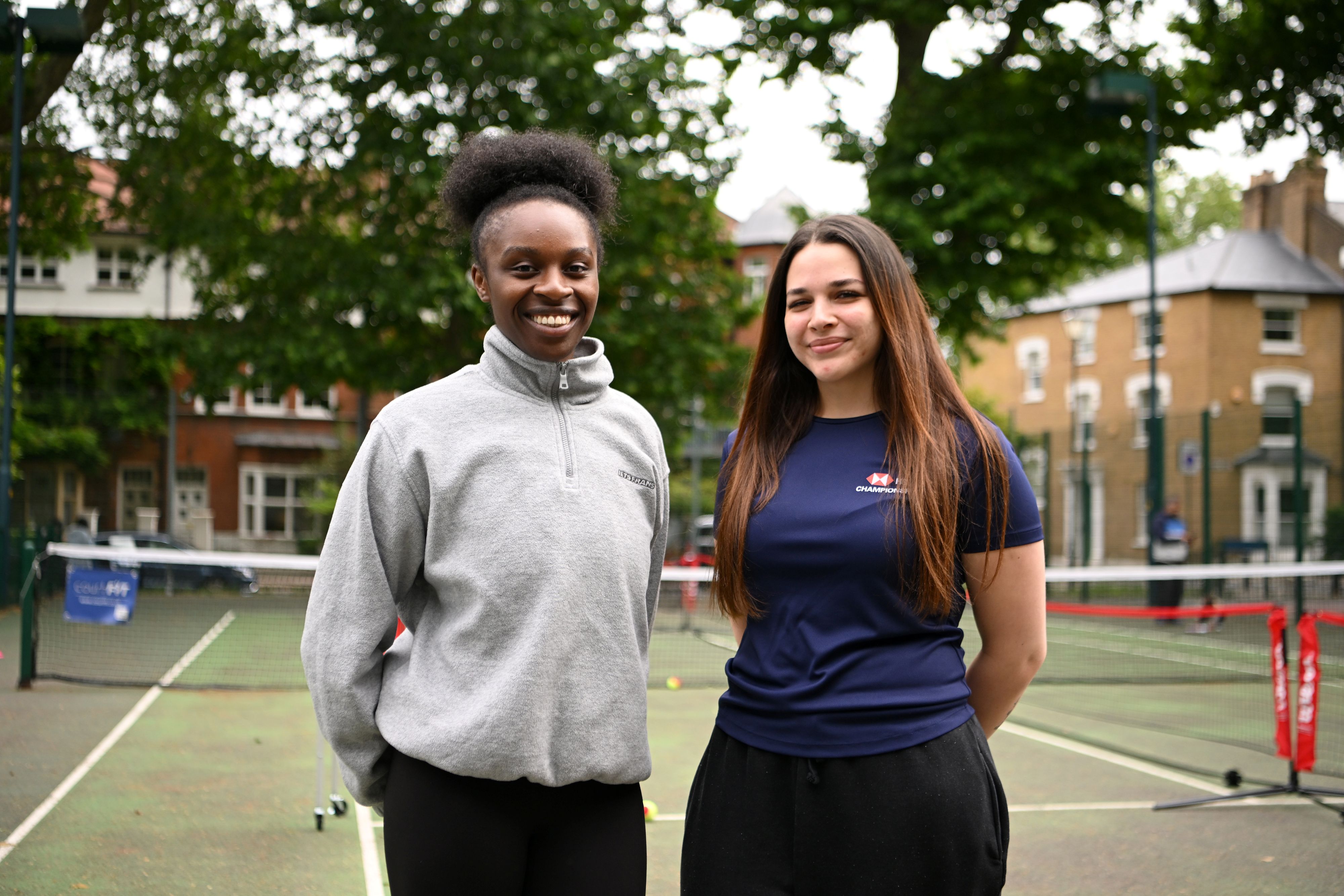 Two females smile on a tennis court