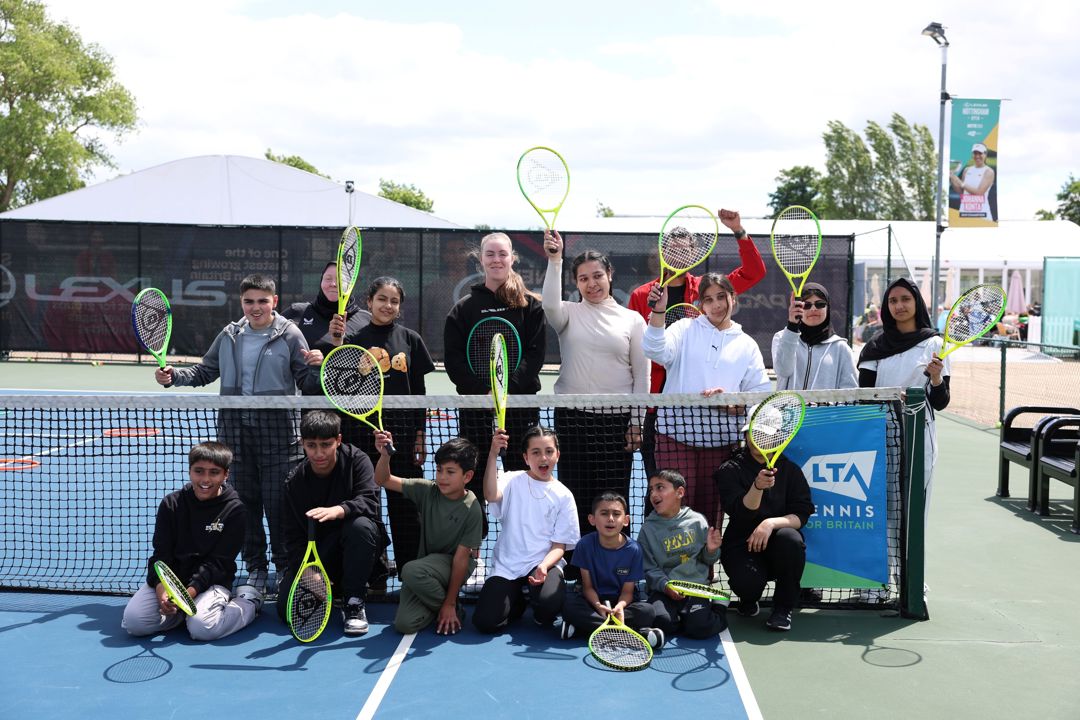 Group of adults and children pose by net on blue tennis court