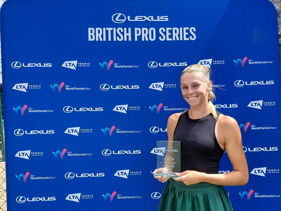 A woman wearing a black vest top and a green sports skirt holds a glass trophy, smiling. Behind her is a blue backdrop featuring the words, 'Lexus British Pro Series', along with a variety of sponsor logos
