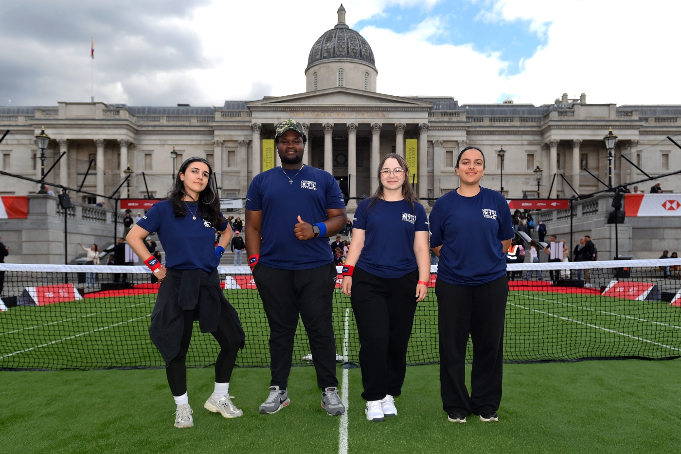 Four people on a tennis court by a net looking at the camera